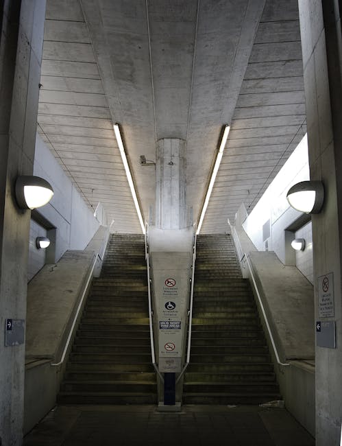 Inside a concrete underground station with a symmetrical staircase leading up from the central walkway, flanked by two sets of stairs on either side. The stairs are made of dark, weathered material, w